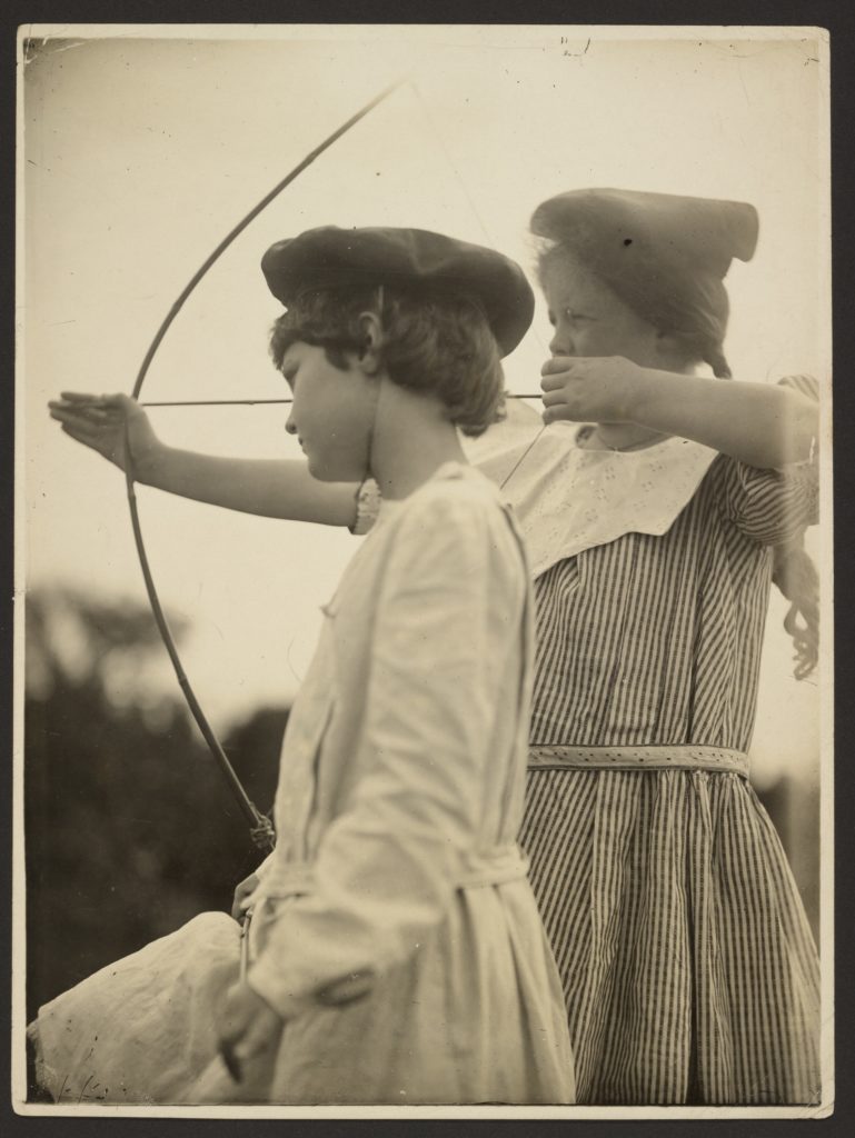Photographie ancienne de deux enfants regardent vers la gauche - l'une tient un arc bandé.