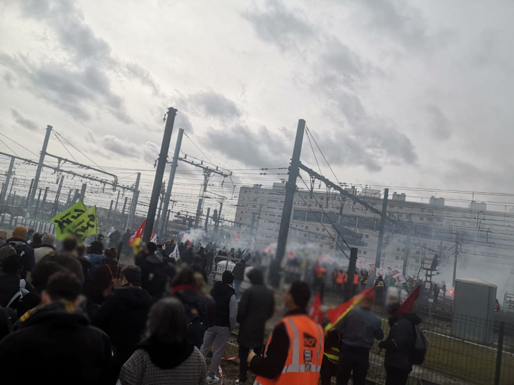 Des manifestants envahissent les voies à gare de Lyon. Il y a de la fumée. On voit un drapeau vert de Sud Rail.