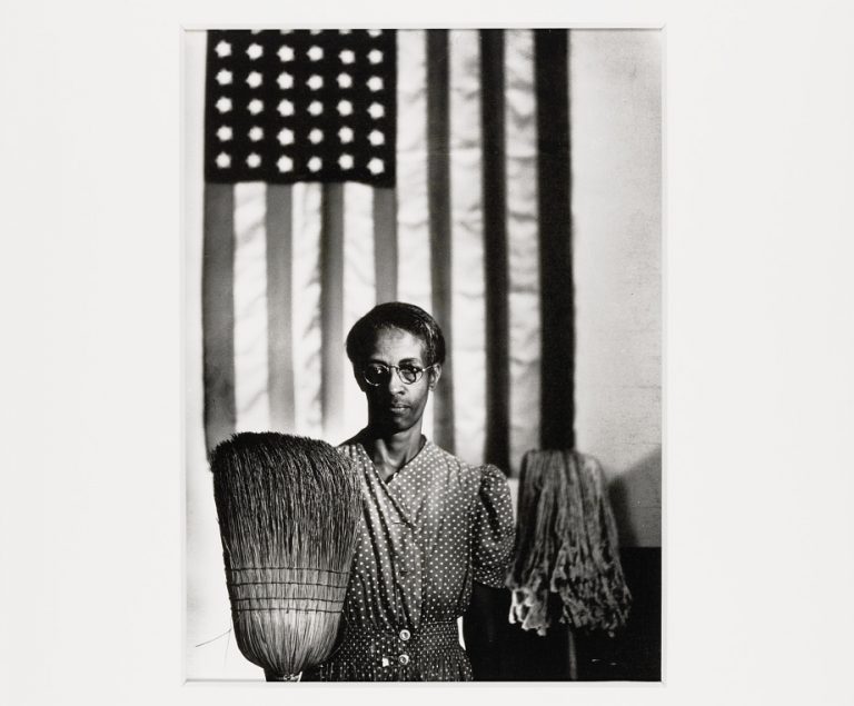femme noire posant avec un balai devant le drapeau américain